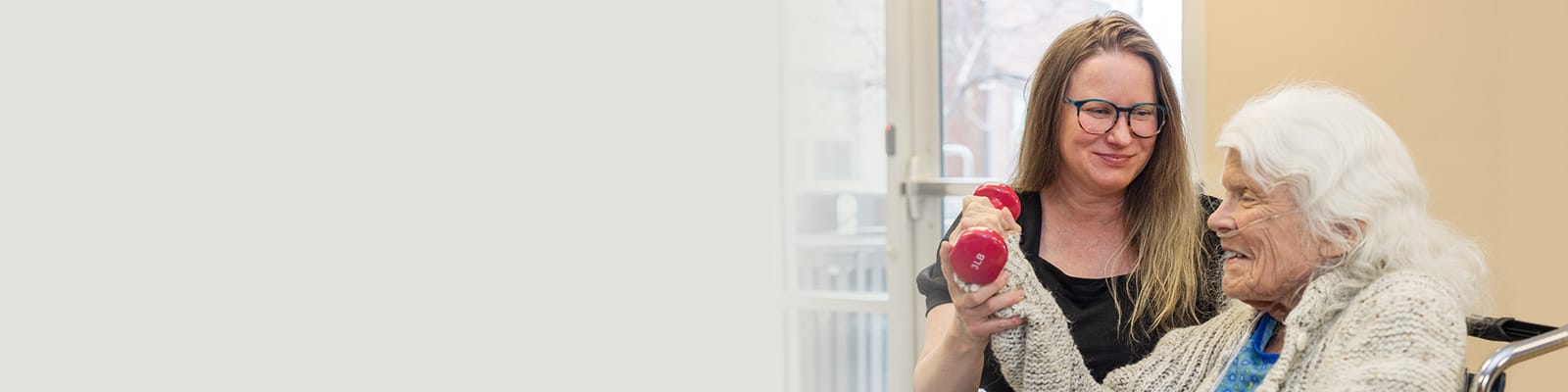 A rehab therapist working with a resident holding a red dumbbell in the rehab gym at Coal Creek Post Acute
